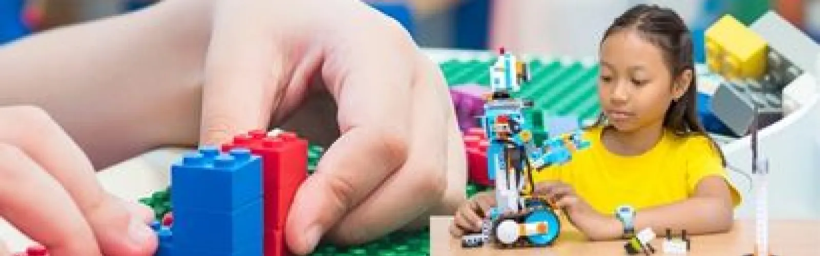 Hands playing with lego, girl in yellow shirt builds with Lego